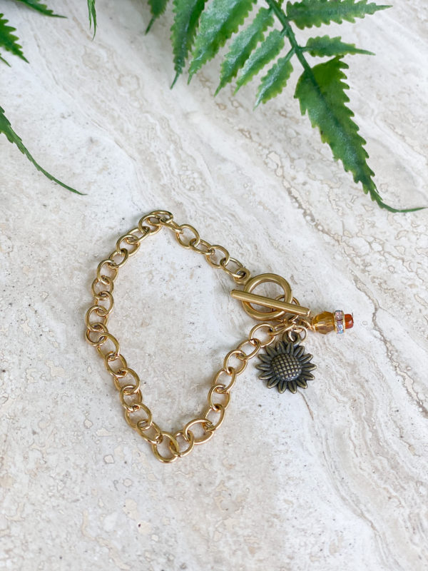 gold sunflower bracelet laying on marble surface